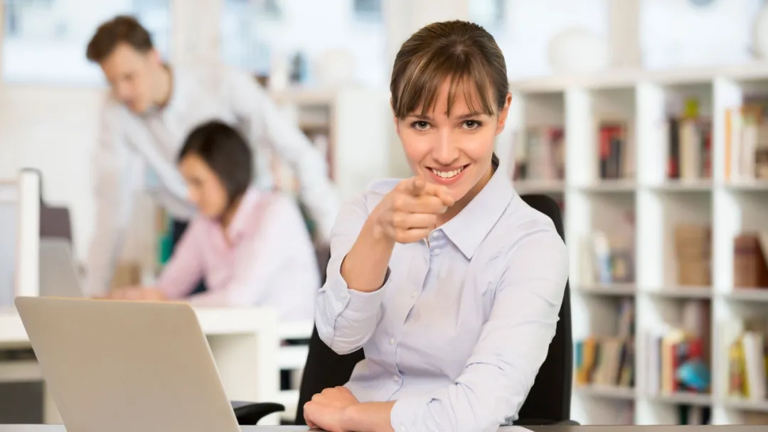 Happy woman at work desk pointing finger