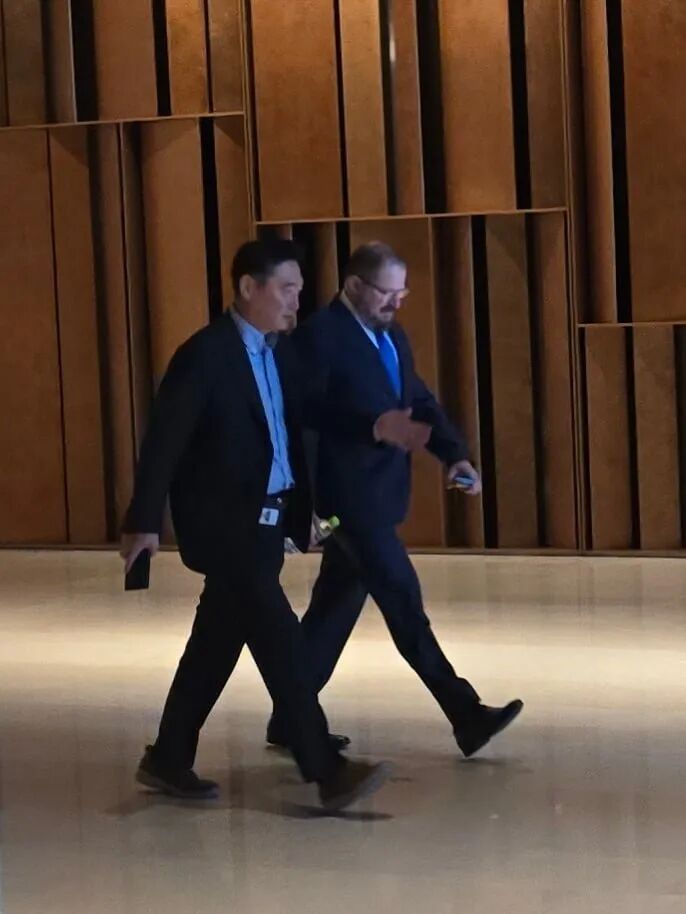 两个穿西装的男人一起走在现代走廊上，走廊里有木质墙板。