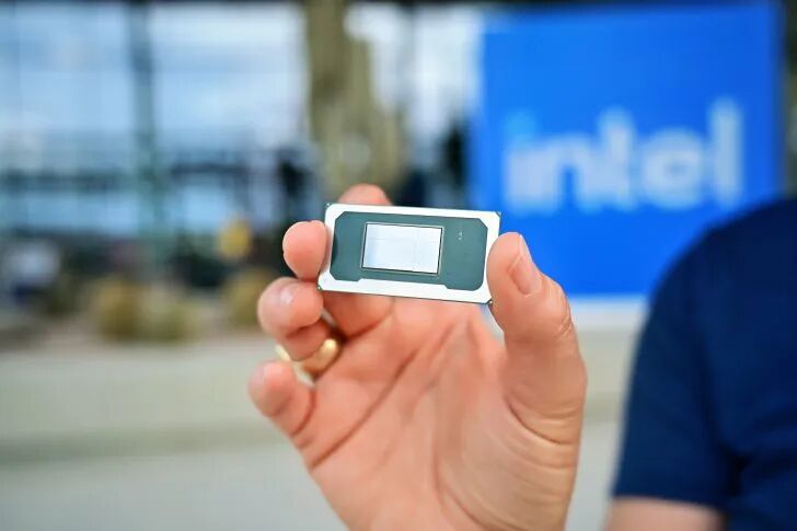 Intel processor held in hand with intel logo in background.